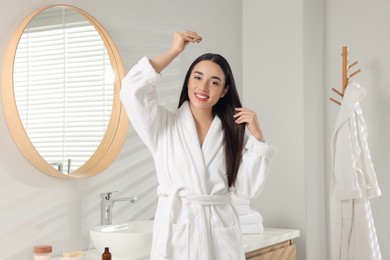 Happy young woman applying essential oil onto hair roots in bathroom