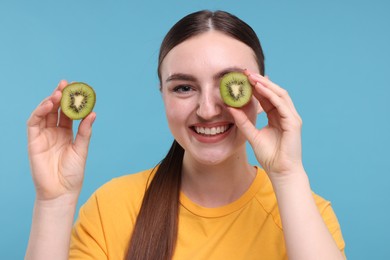 Photo of Smiling woman covering eye with half of kiwi on light blue background