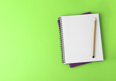 Notebooks with pencil on light green background, top view. Space for text