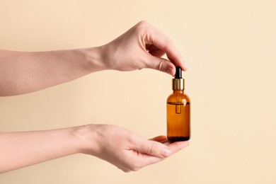 Photo of Woman holding bottle of cosmetic oil on beige background, closeup