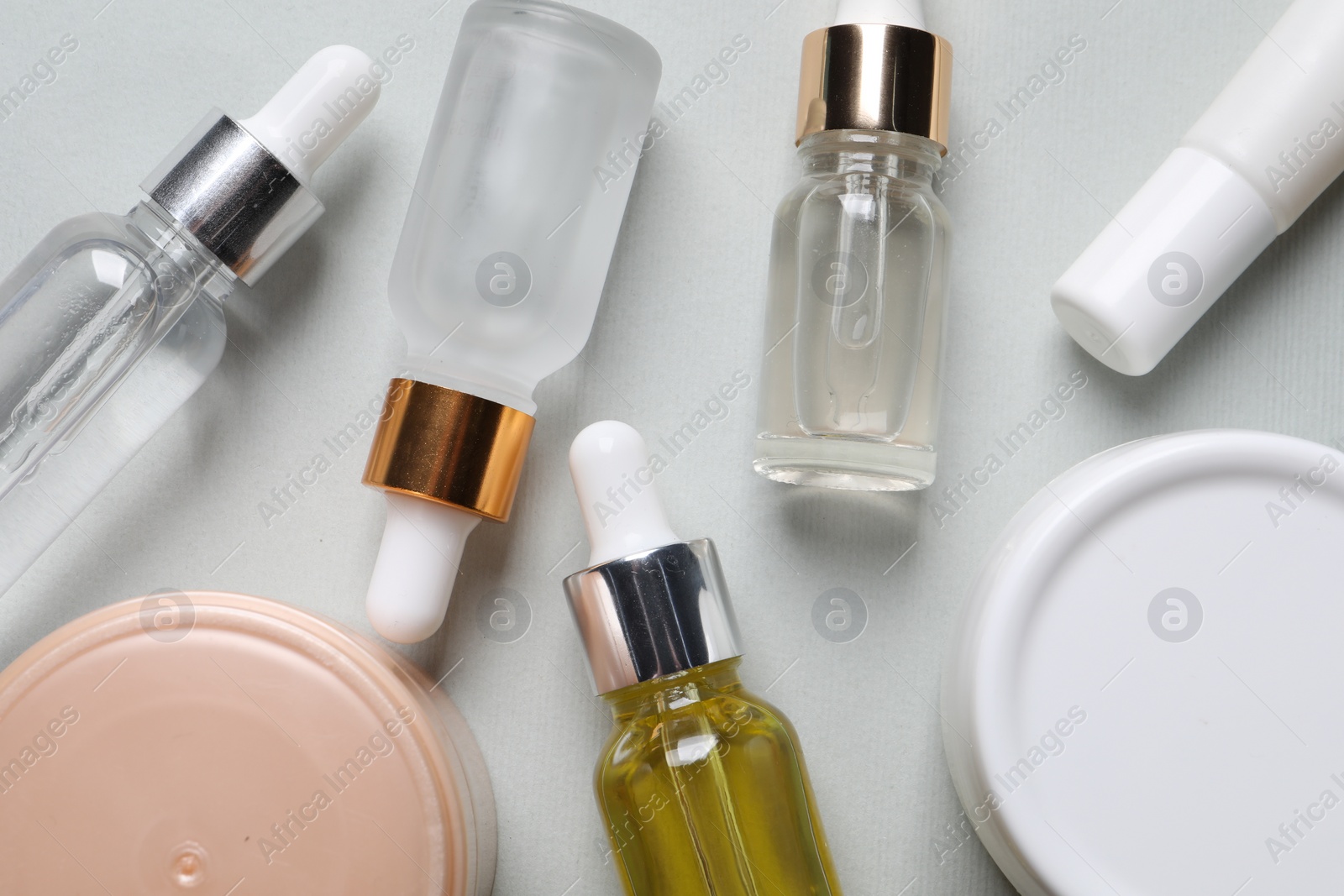 Photo of Many bottles and tube of cosmetic serum on light grey background, flat lay