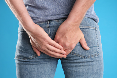 Photo of Man suffering from hemorrhoid on light blue background, closeup