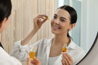 Photo of Young woman with bottle of essential oil near mirror indoors