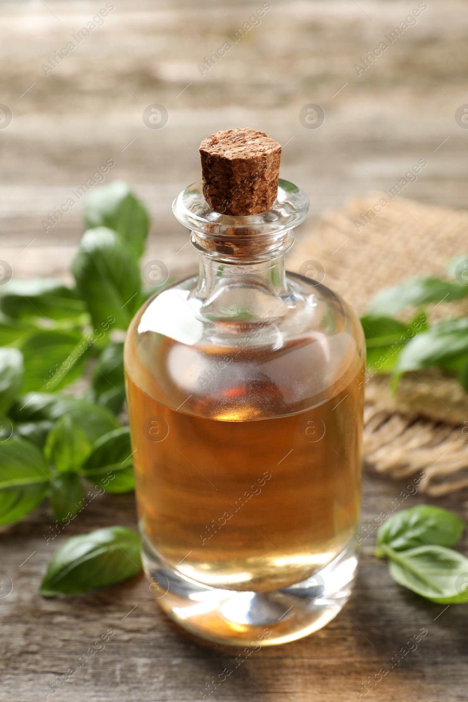 Photo of Glass bottle of basil essential oil and leaves on wooden table, closeup