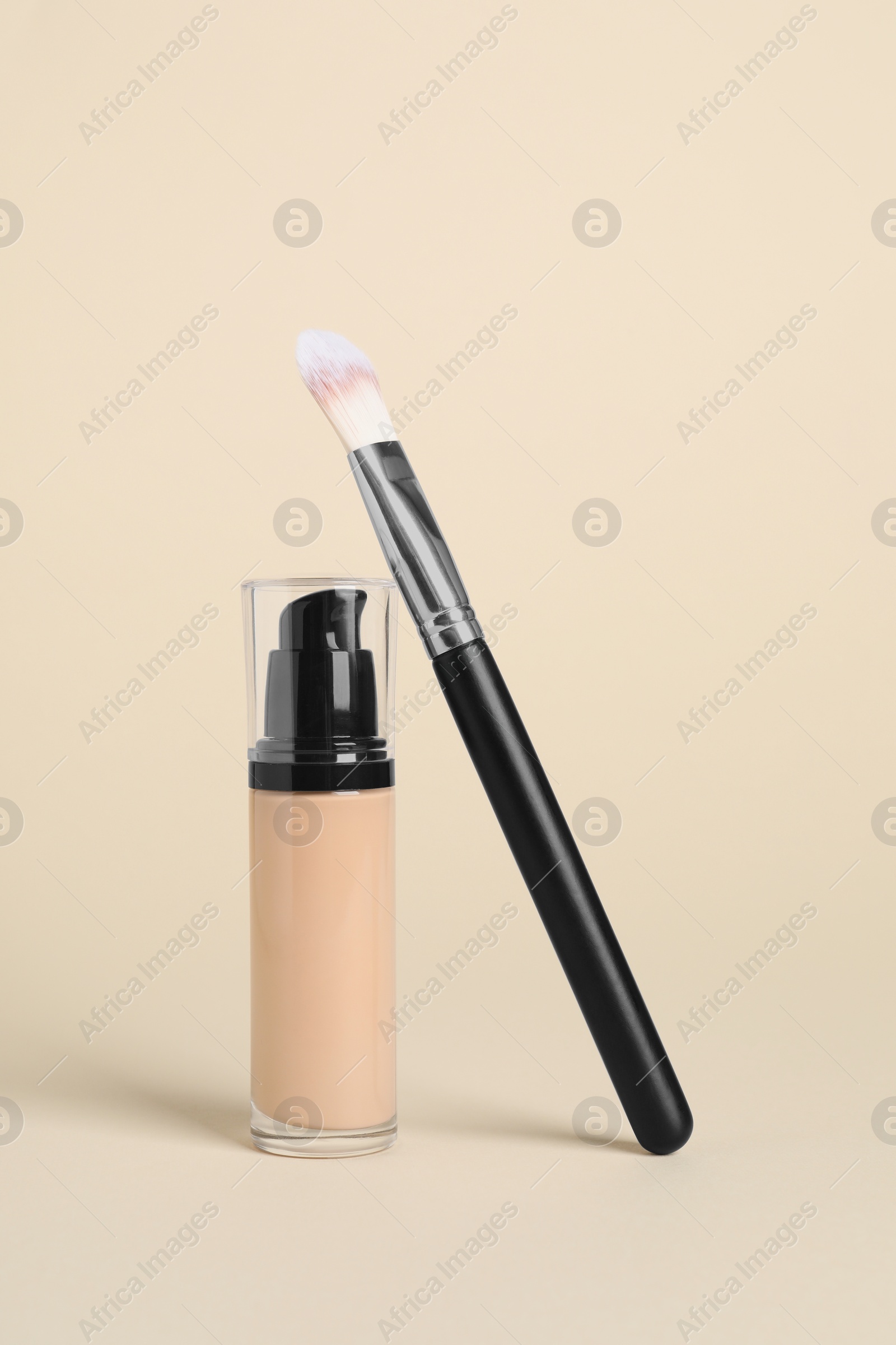 Photo of Bottle of skin foundation and brush on beige background. Makeup product