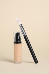 Photo of Bottle of skin foundation and brush on beige background. Makeup product