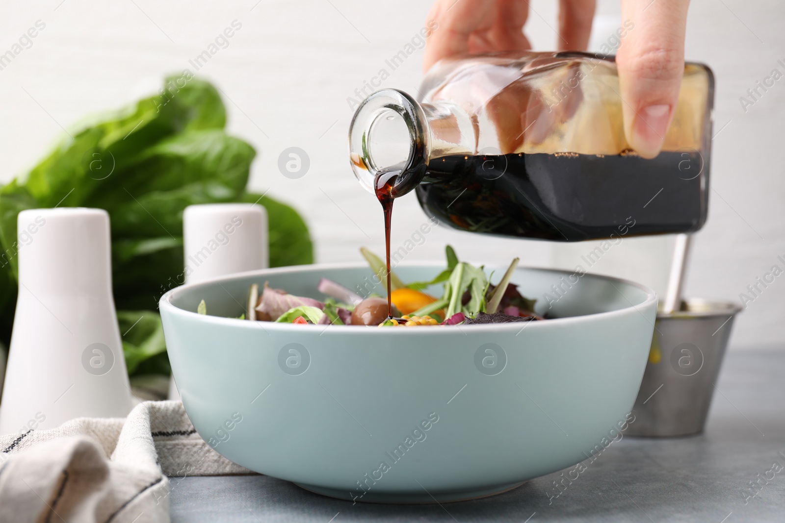 Photo of Pouring vinegar from bottle into bowl with salad at grey table, closeup