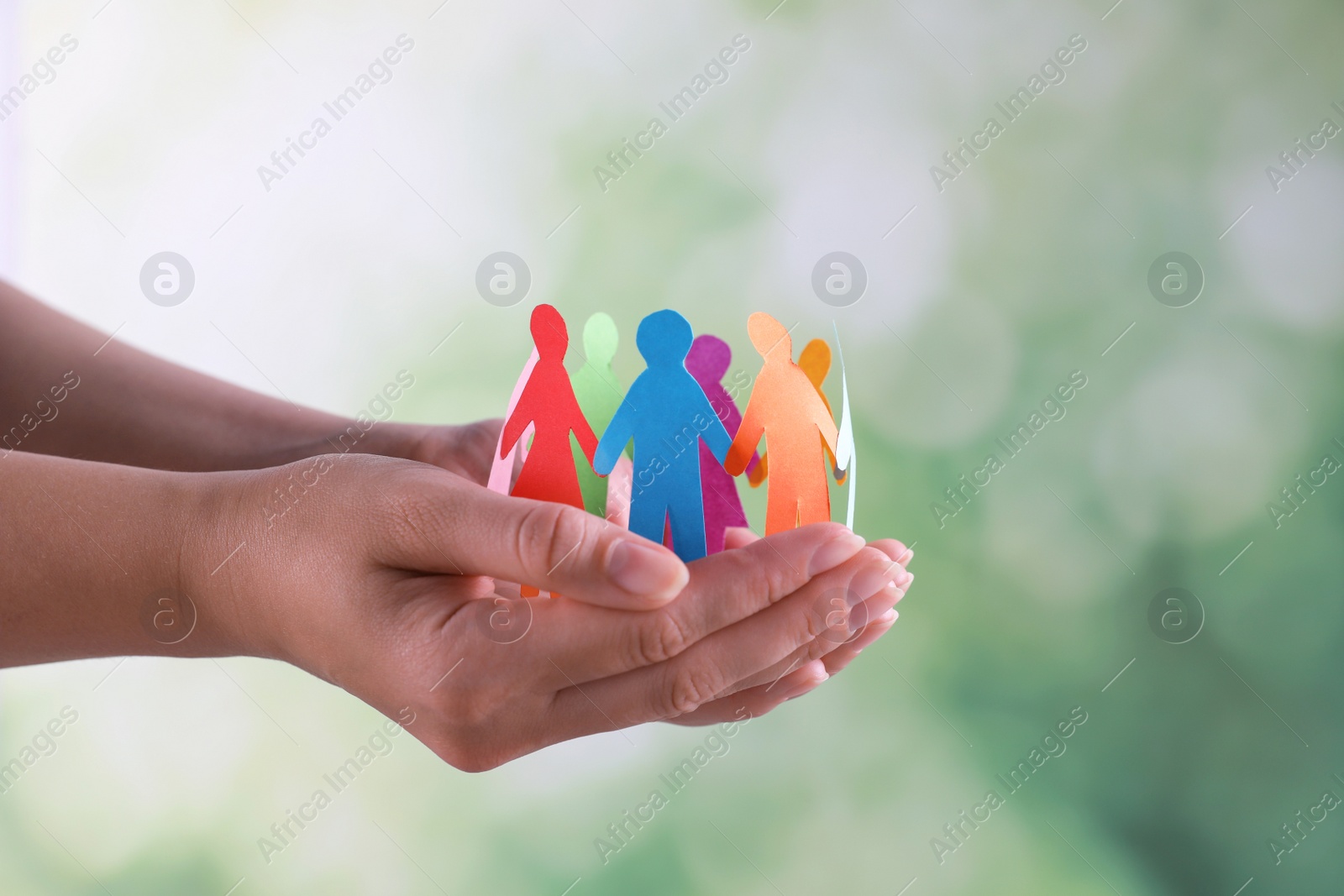 Photo of Woman holding paper human figures on blurred background, closeup. Diversity and Inclusion concept