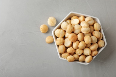 Photo of Bowl with shelled organic Macadamia nuts and space for text on grey background, top view