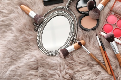 Photo of Flat lay composition with makeup brushes, cosmetic products and mirror on faux fur