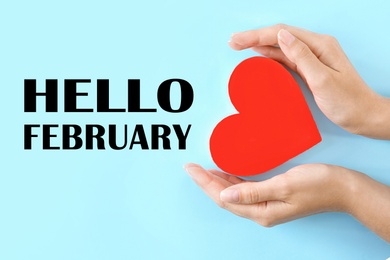 Image of Greeting card with text Hello February, Woman holding hands near red heart on light blue background, closeup