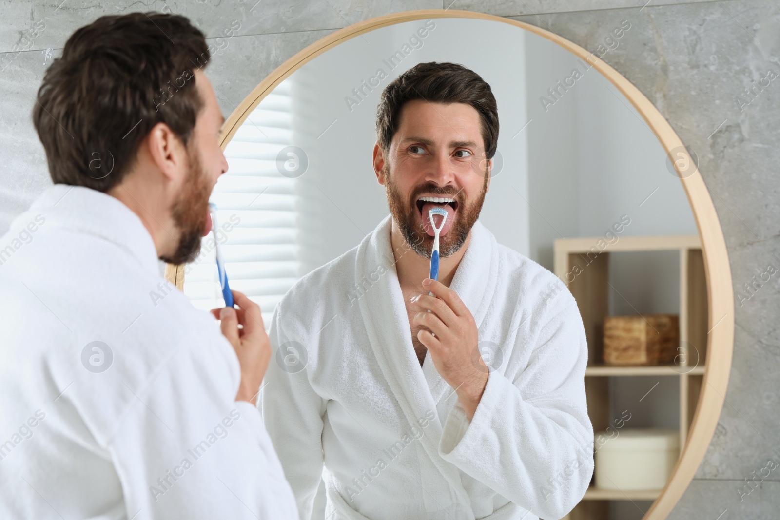 Photo of Handsome man brushing his tongue with cleaner near mirror in bathroom