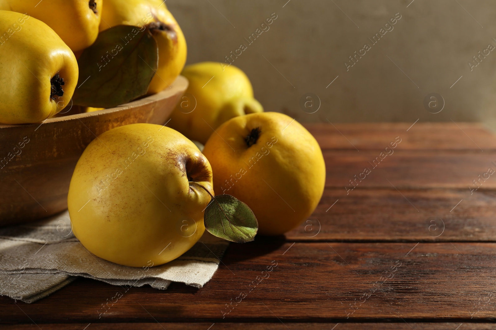 Photo of Tasty ripe quince fruits in bowl on wooden table, closeup. Space for text