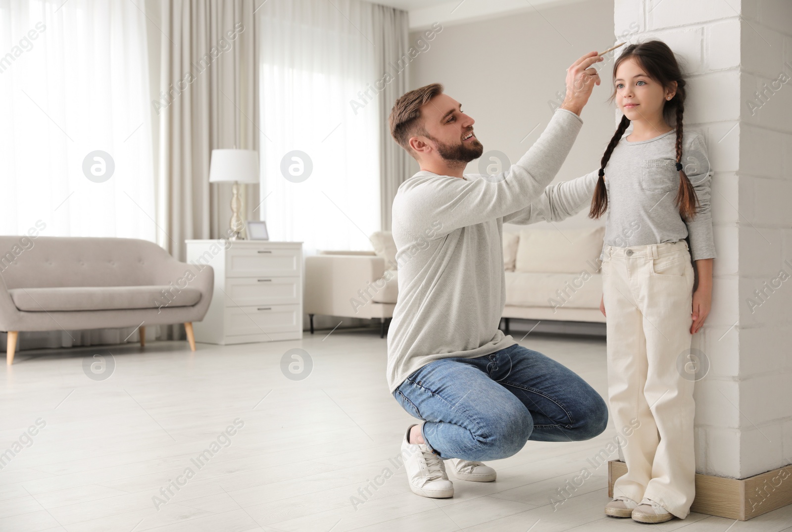 Photo of Father measuring daughter's height near white brick pillar at home, space for text