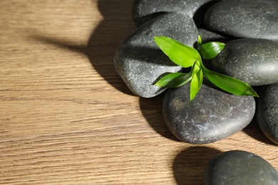 Photo of Pile of spa stones and green leaves on wooden table, space for text