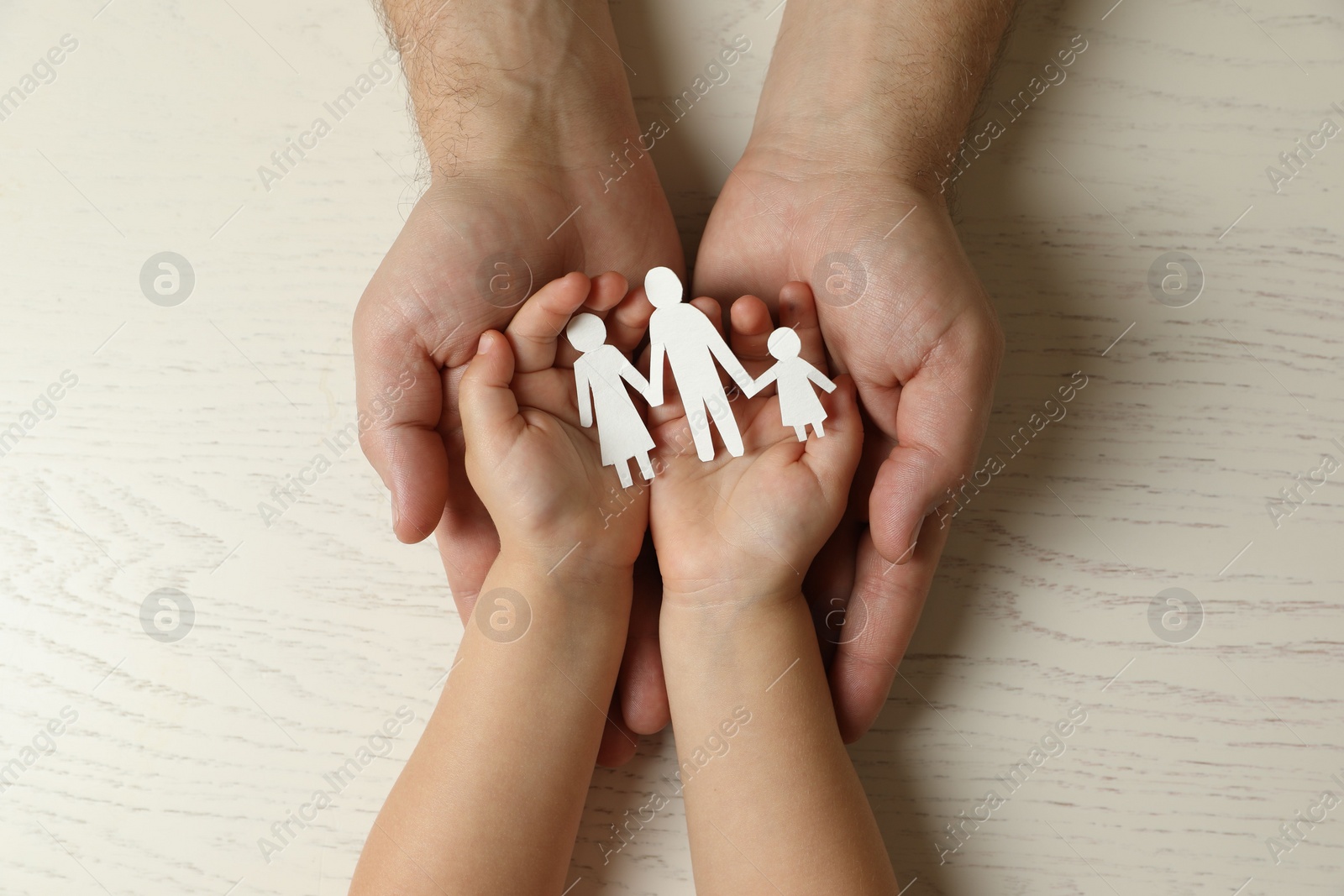 Photo of Father and child holding paper cutout of family at white wooden table, top view