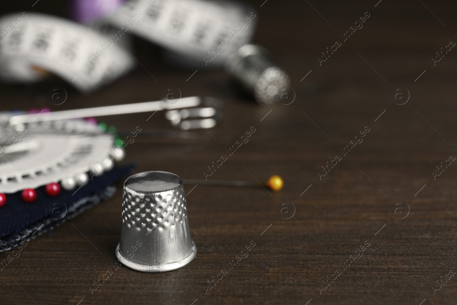 Photo of Silver thimble on wooden table, space for text. Sewing accessory