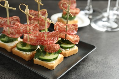 Tasty canapes with salami, cucumber and cream cheese on grey table, closeup. Space for text