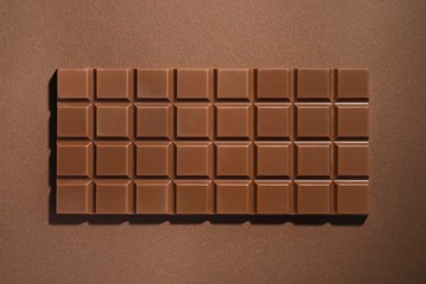 Tasty chocolate bar on brown background, top view