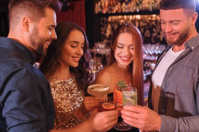 Photo of Happy friends clinking glasses with fresh cocktails in bar