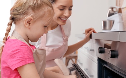 Mother and her daughter baking food in oven at home