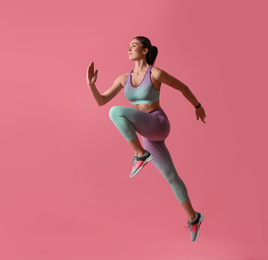 Photo of Athletic young woman running on pink background, side view