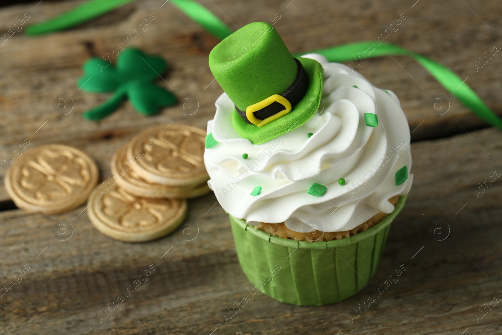 Photo of St. Patrick's day party. Tasty cupcake with green leprechaun hat topper on wooden table, closeup