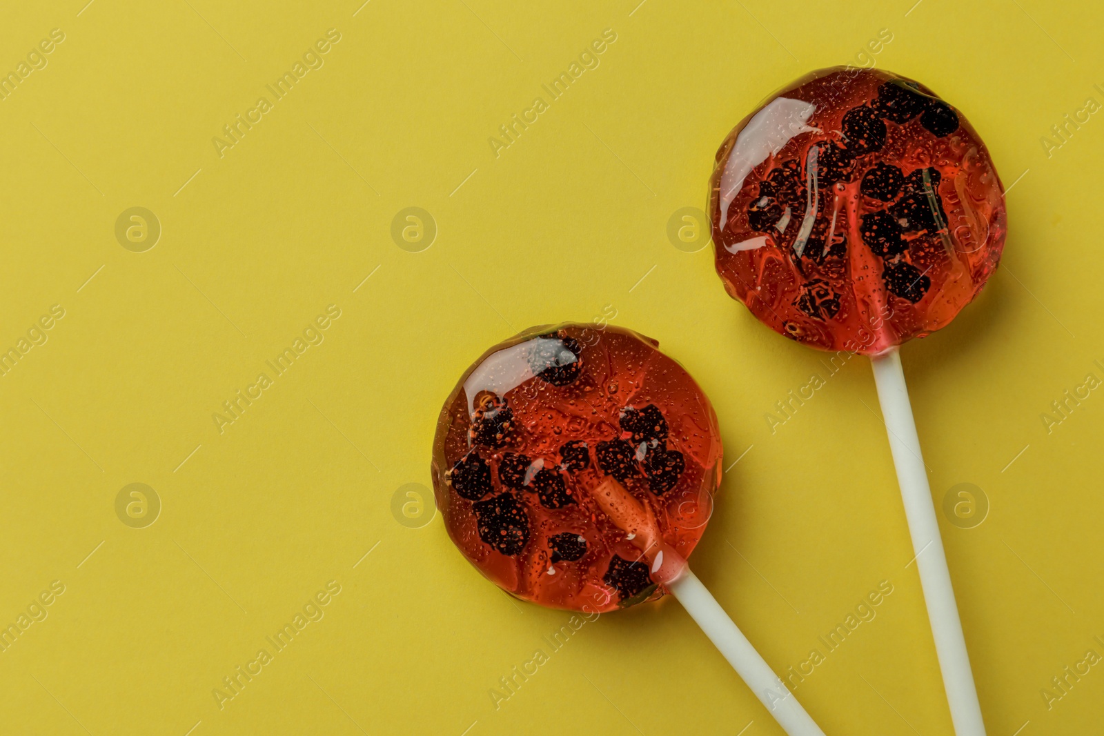 Photo of Sweet colorful lollipops with berries on yellow background, flat lay. Space for text