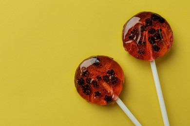 Sweet colorful lollipops with berries on yellow background, flat lay. Space for text