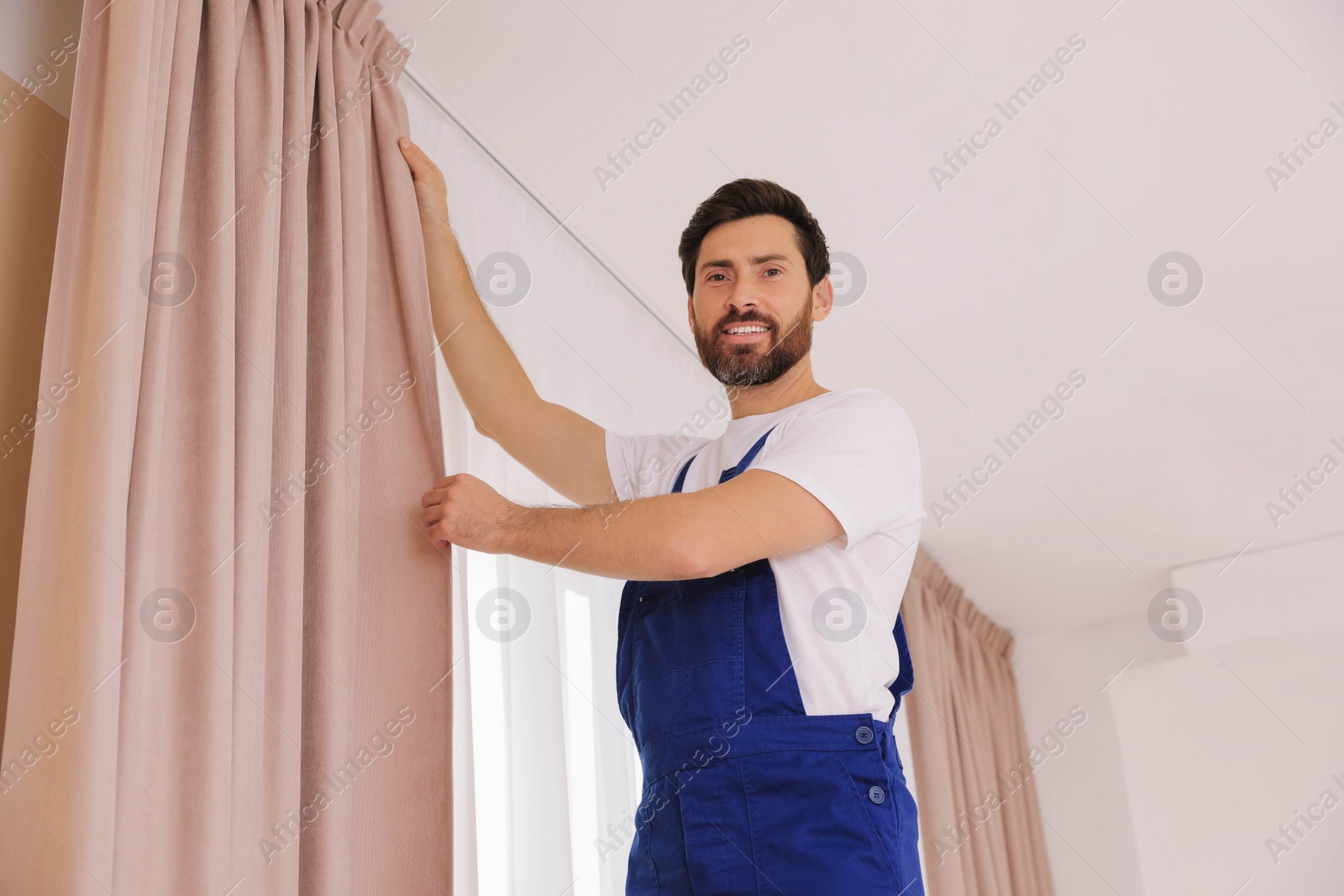 Photo of Worker in uniform hanging window curtain indoors