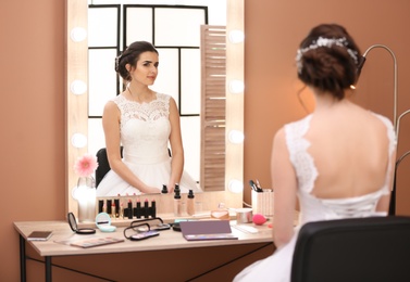 Photo of Beautiful young bride with makeup made by professional artist near mirror in salon