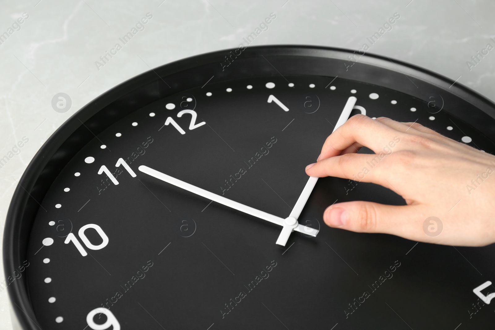 Photo of Woman changing time on big black clock, closeup