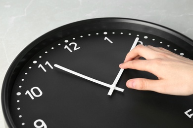 Photo of Woman changing time on big black clock, closeup