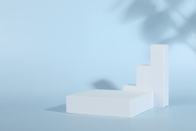 Photo of Presentation of product. Podiums and shadows on light blue background. Space for text