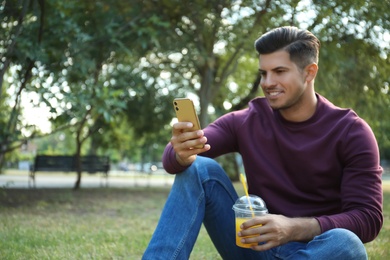 Photo of Man with smartphone and refreshing drink in park