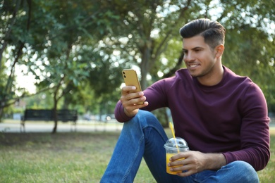 Man with smartphone and refreshing drink in park