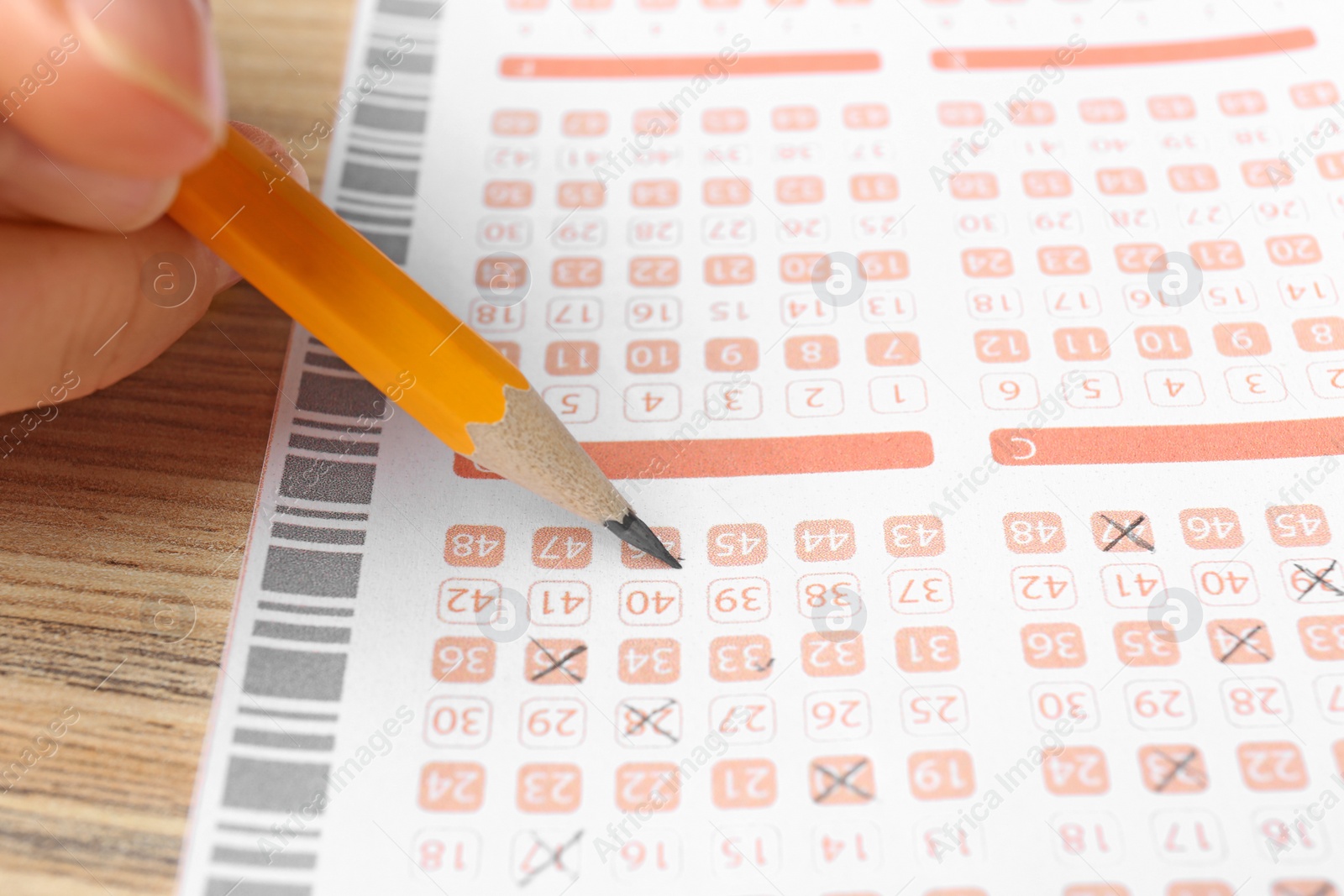 Photo of Woman filling out lottery ticket with pencil on wooden table, closeup. Space for text