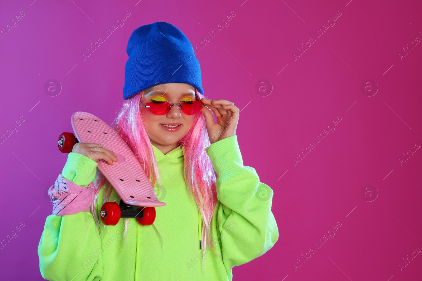 Photo of Cute indie girl with penny board on violet background, space for text