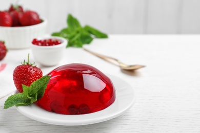 Photo of Delicious fresh red jelly with berries and mint on white wooden table, space for text
