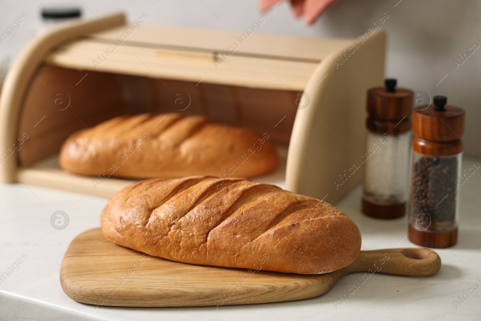 Photo of Wooden bread basket with freshly baked loaves on white marble table in kitchen