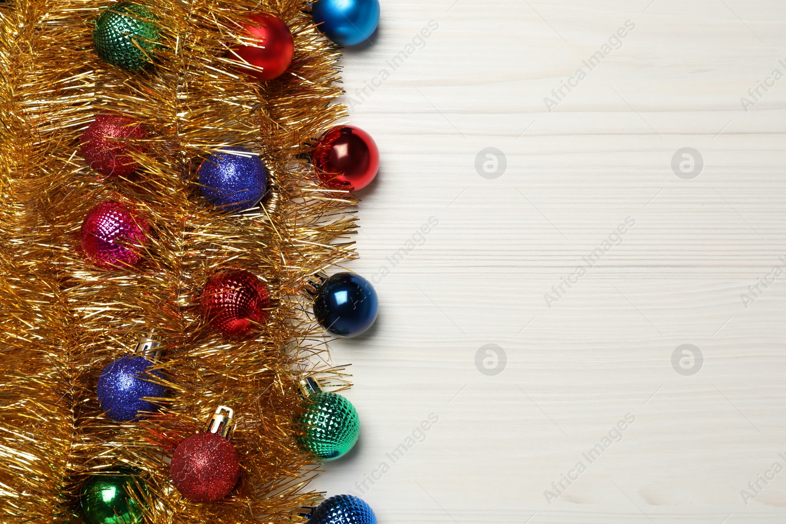 Photo of Shiny golden tinsel with Christmas balls on white wooden background, flat lay. Space for text