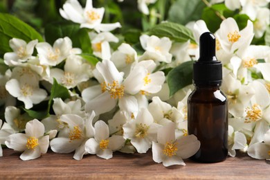 Photo of Jasmine essential oil and fresh flowers on wooden table, space for text