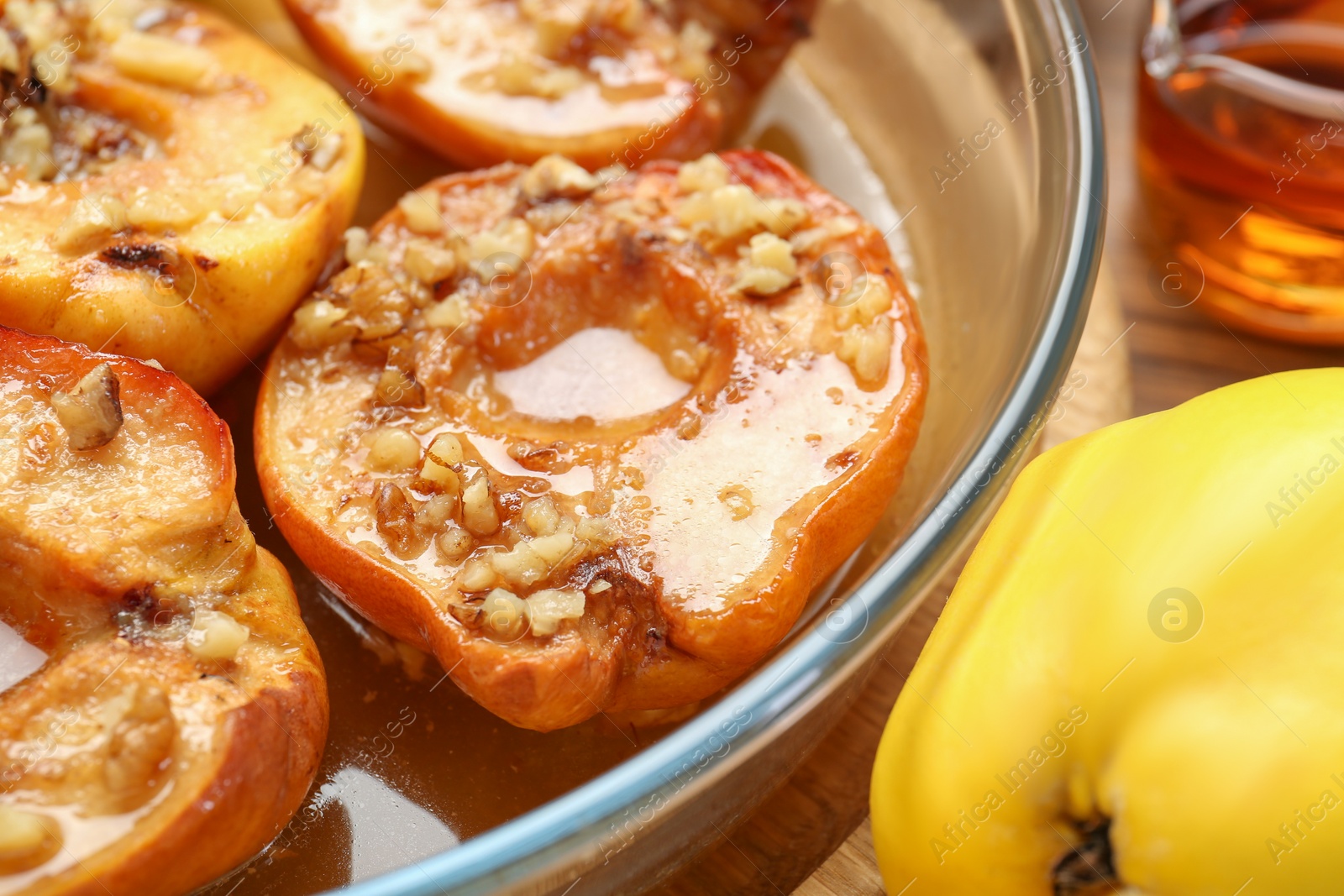 Photo of Tasty baked quinces with walnuts and honey in bowl on wooden table, closeup