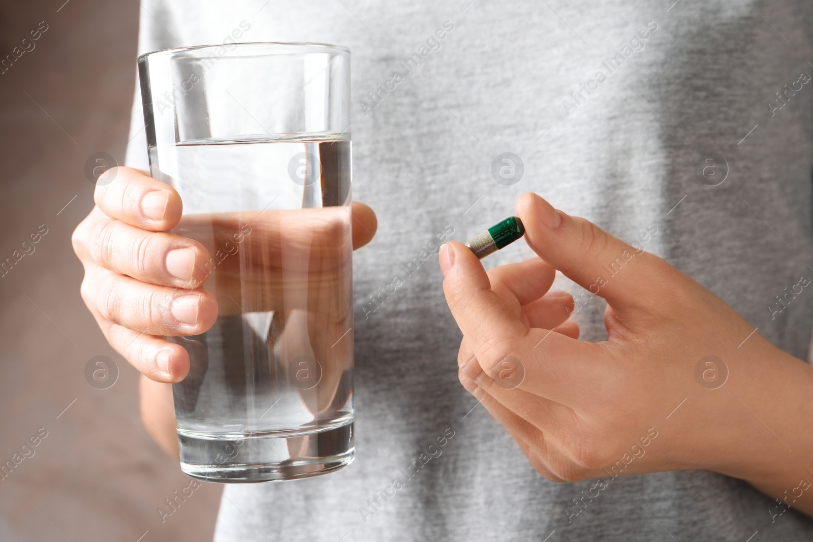 Photo of Woman holding spirulina pill and glass of water, closeup