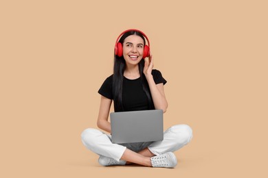 Photo of Happy woman with laptop listening to music in headphones on beige background