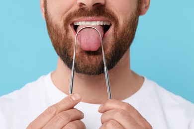 Photo of Man brushing his tongue with cleaner on light blue background, closeup