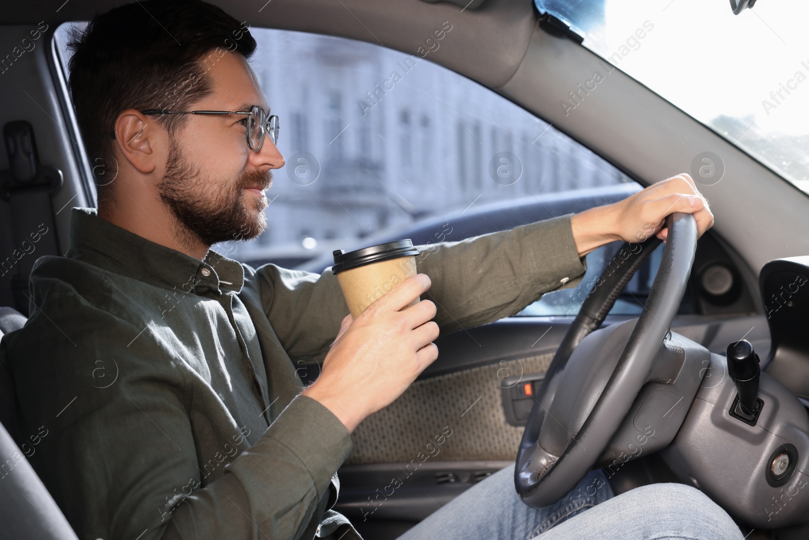 Photo of Coffee to go. Handsome man with paper cup of drink driving his car