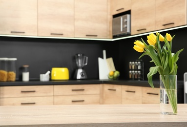 Glass vase with tulips on table in kitchen