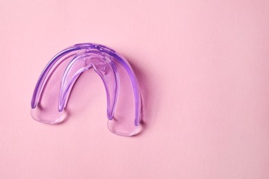 Photo of Transparent dental mouth guard on light pink background, top view with space for text. Bite correction