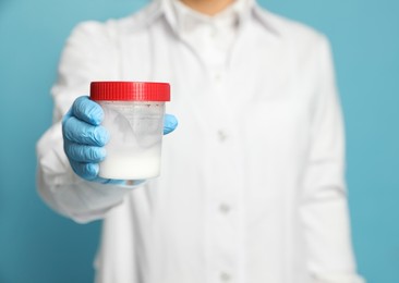 Scientist holding container with sperm on turquoise background, closeup. Space for text
